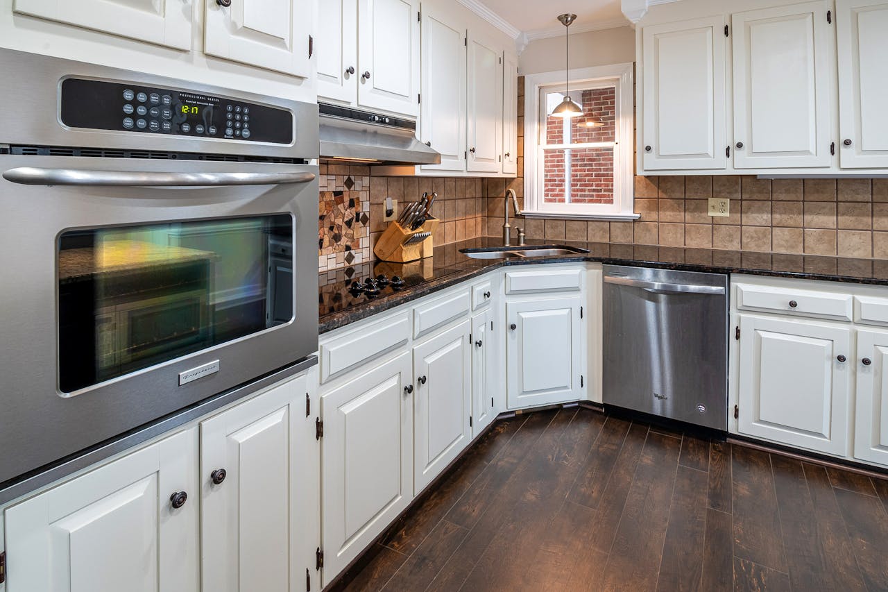 Spacious kitchen featuring white cabinets, stainless steel appliances, and wooden flooring.