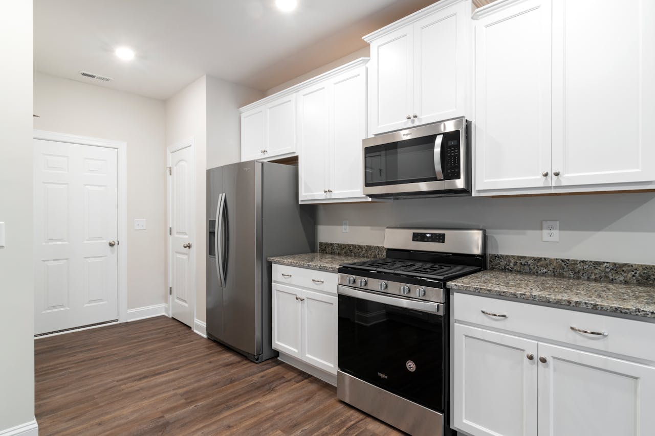 services-04 Contemporary kitchen featuring stainless steel fridge and microwave with white cabinetry.
